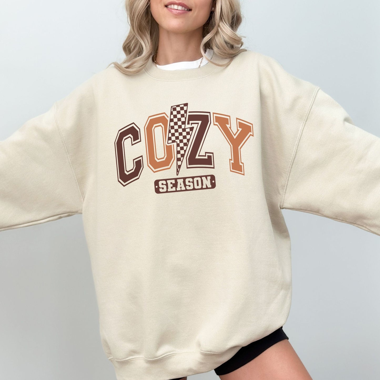 Person wearing a beige sweatshirt with 'COZY SEASON' text and checkered design on a plain background