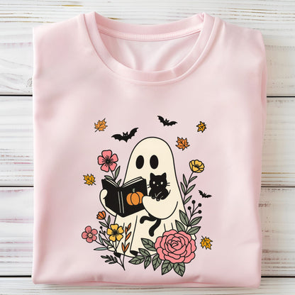 Folded pink t-shirt with Halloween-themed design featuring a ghost, cat, and pumpkins on a wooden surface.
