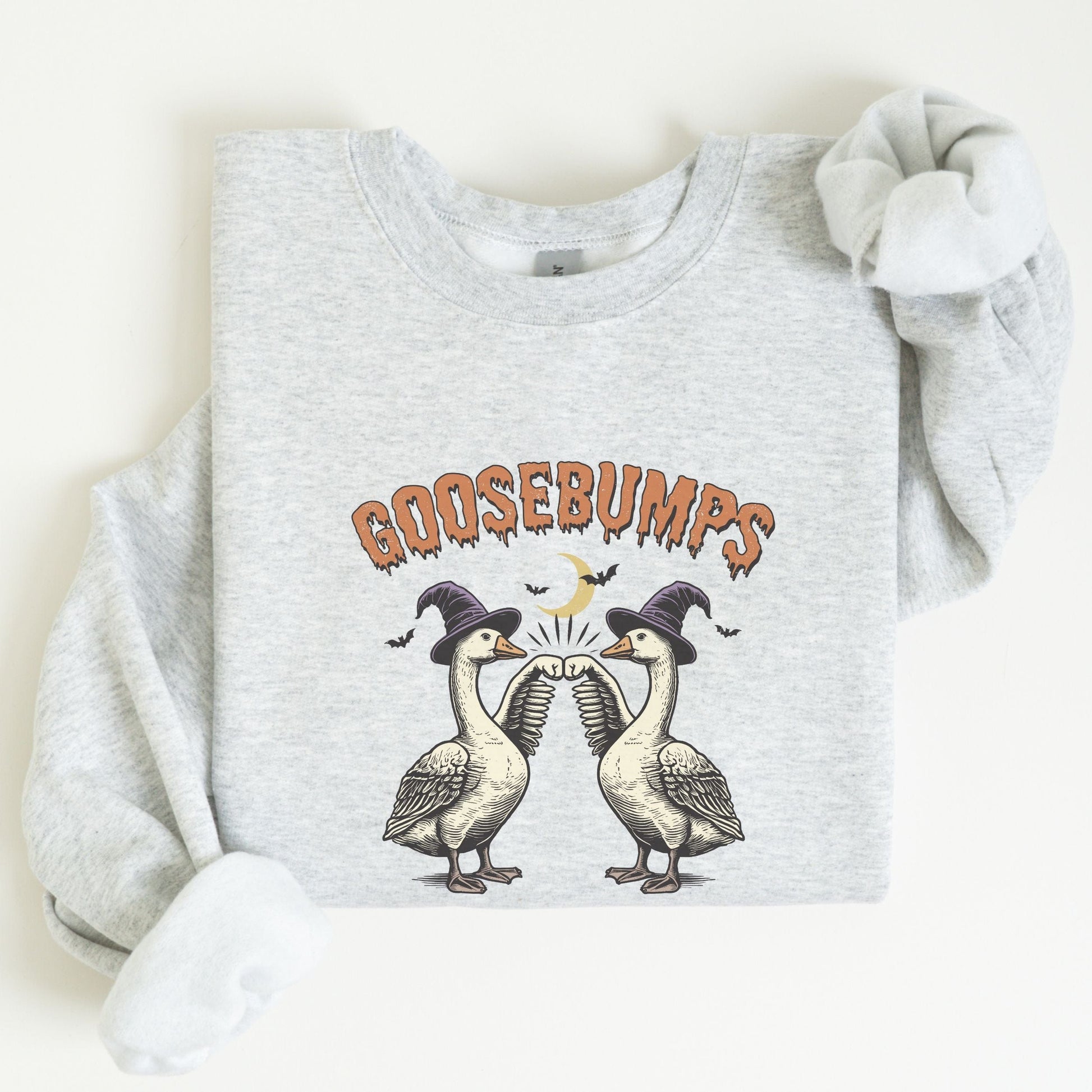 Halloween sweatshirt with two geese in witch hats bumping wings under a crescent moon — spooky and fun fall apparel.