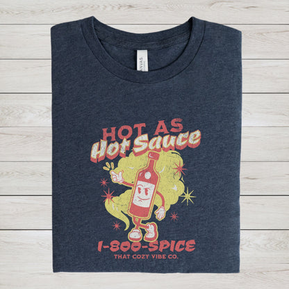 “Hot As Hot Sauce” t-shirt with retro cartoon hot sauce bottle character, bold yellow and red text, spice cloud, and “1-800-SPICE” at the bottom.