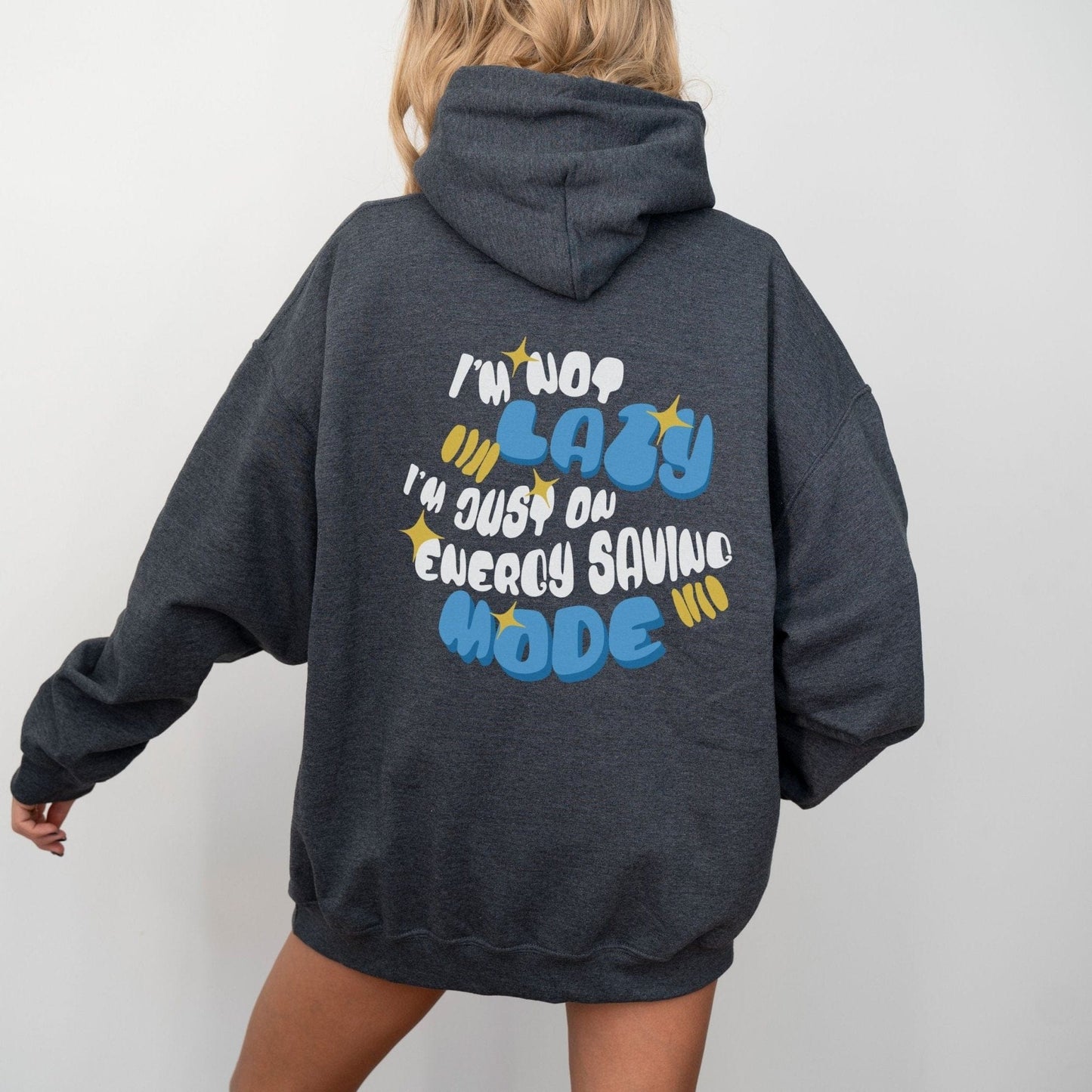 Back of a hoodie with the phrase “I’m Not Lazy, I’m Just on Energy Saving Mode” in playful retro typography. Cozy, unisex fit.