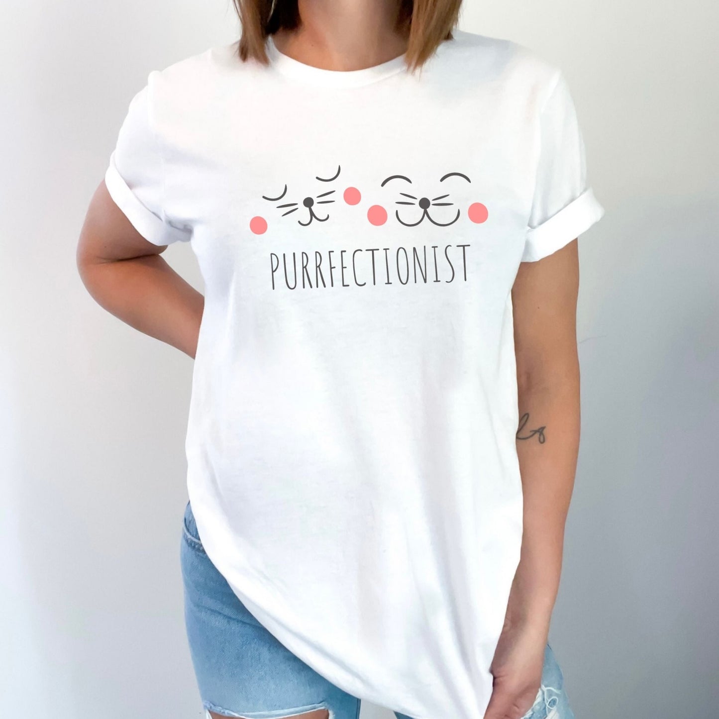 Shirt with "Purrfectionist" text and cute cat face design for cat lovers.