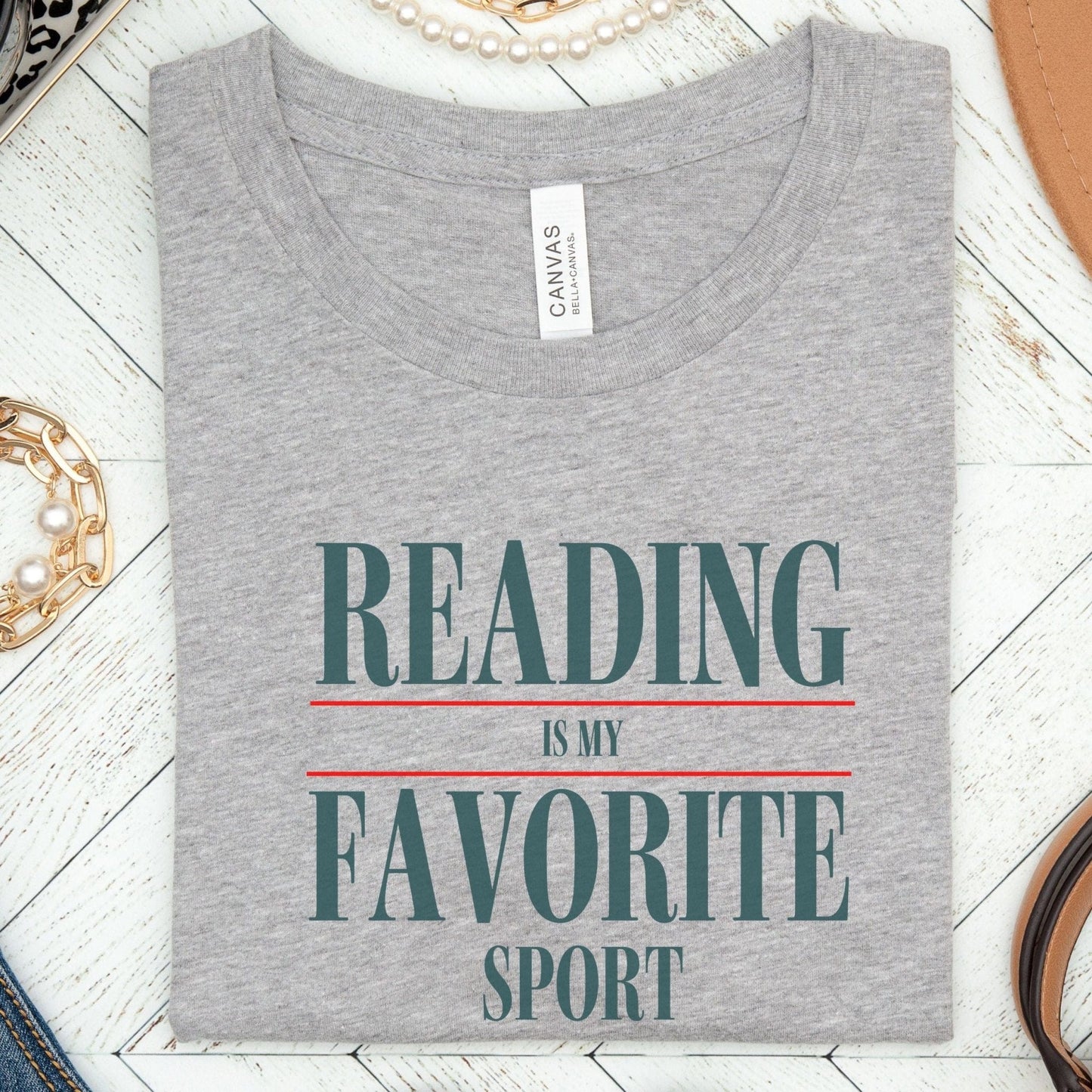 “Reading Is My Favorite Sport” t-shirt with bold serif font in dark teal and red underline accents, minimalist literary design.