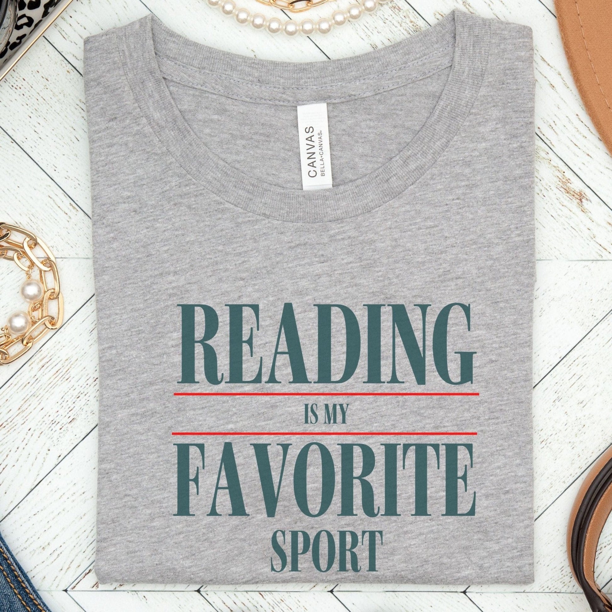 “Reading Is My Favorite Sport” t-shirt with bold serif font in dark teal and red underline accents, minimalist literary design.
