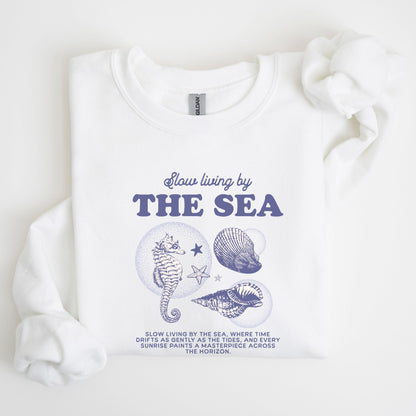 Vintage-style seahorse and seashell graphic with “Slow Living by the Sea” text on a soft unisex sweatshirt, part of the summer coastal collection.