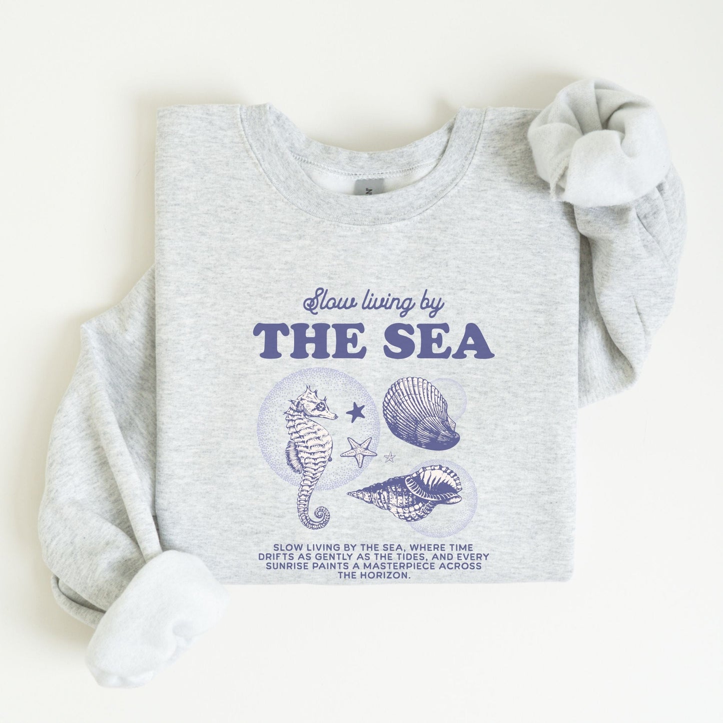 Vintage-style seahorse and seashell graphic with “Slow Living by the Sea” text on a soft unisex sweatshirt, part of the summer coastal collection.