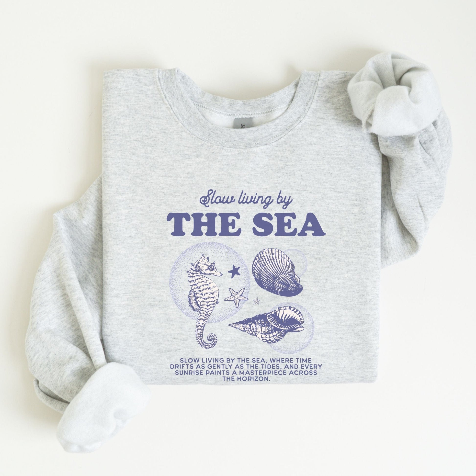Vintage-style seahorse and seashell graphic with “Slow Living by the Sea” text on a soft unisex sweatshirt, part of the summer coastal collection.