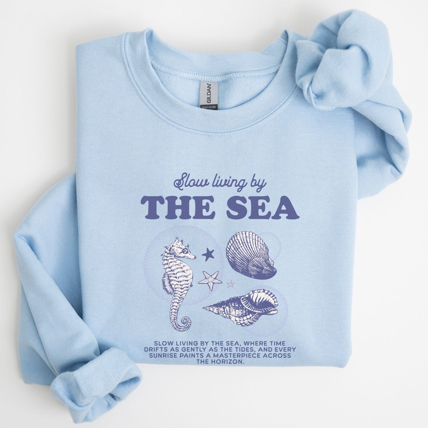 Vintage-style seahorse and seashell graphic with “Slow Living by the Sea” text on a soft unisex sweatshirt, part of the summer coastal collection.