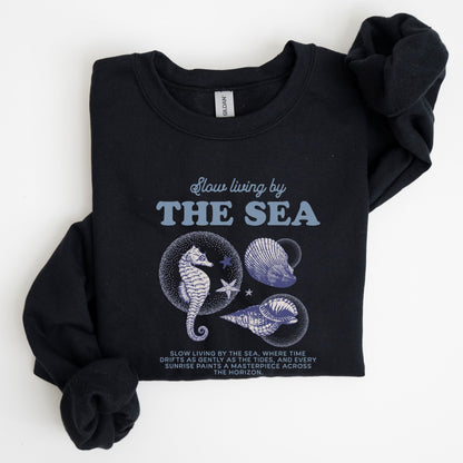 Vintage-style seahorse and seashell graphic with “Slow Living by the Sea” text on a soft unisex sweatshirt, part of the summer coastal collection.