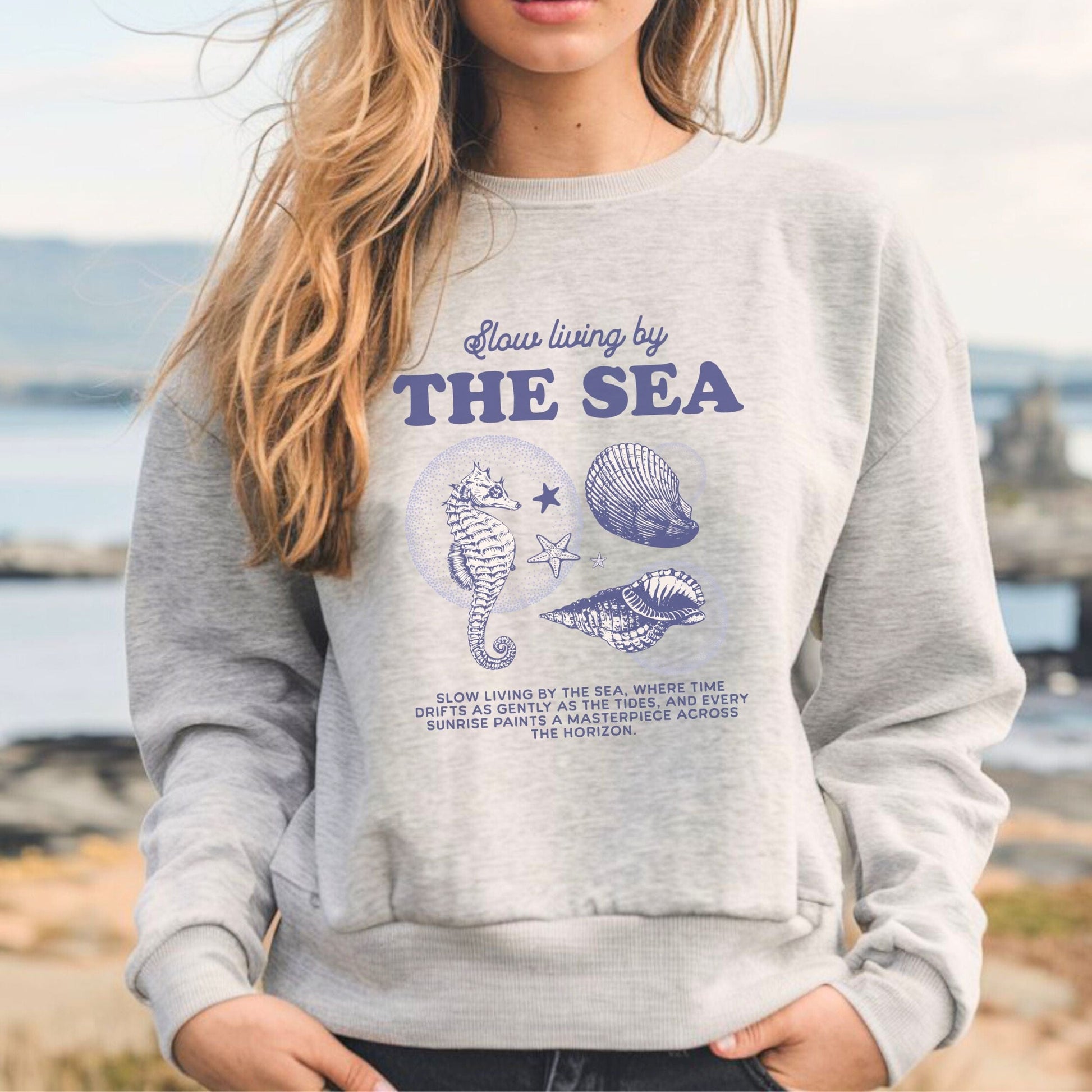 Vintage-style seahorse and seashell graphic with “Slow Living by the Sea” text on a soft unisex sweatshirt, part of the summer coastal collection.