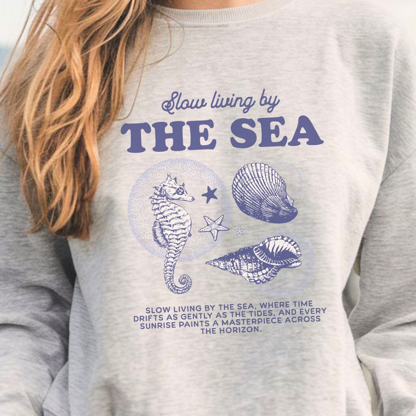 Vintage-style seahorse and seashell graphic with “Slow Living by the Sea” text on a soft unisex sweatshirt, part of the summer coastal collection.