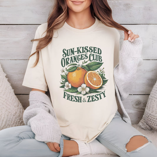 T-shirt design with vintage "Sun-Kissed Oranges Club" text, featuring a bright orange with blossoms and greenery, labeled “Fresh & Zesty.”