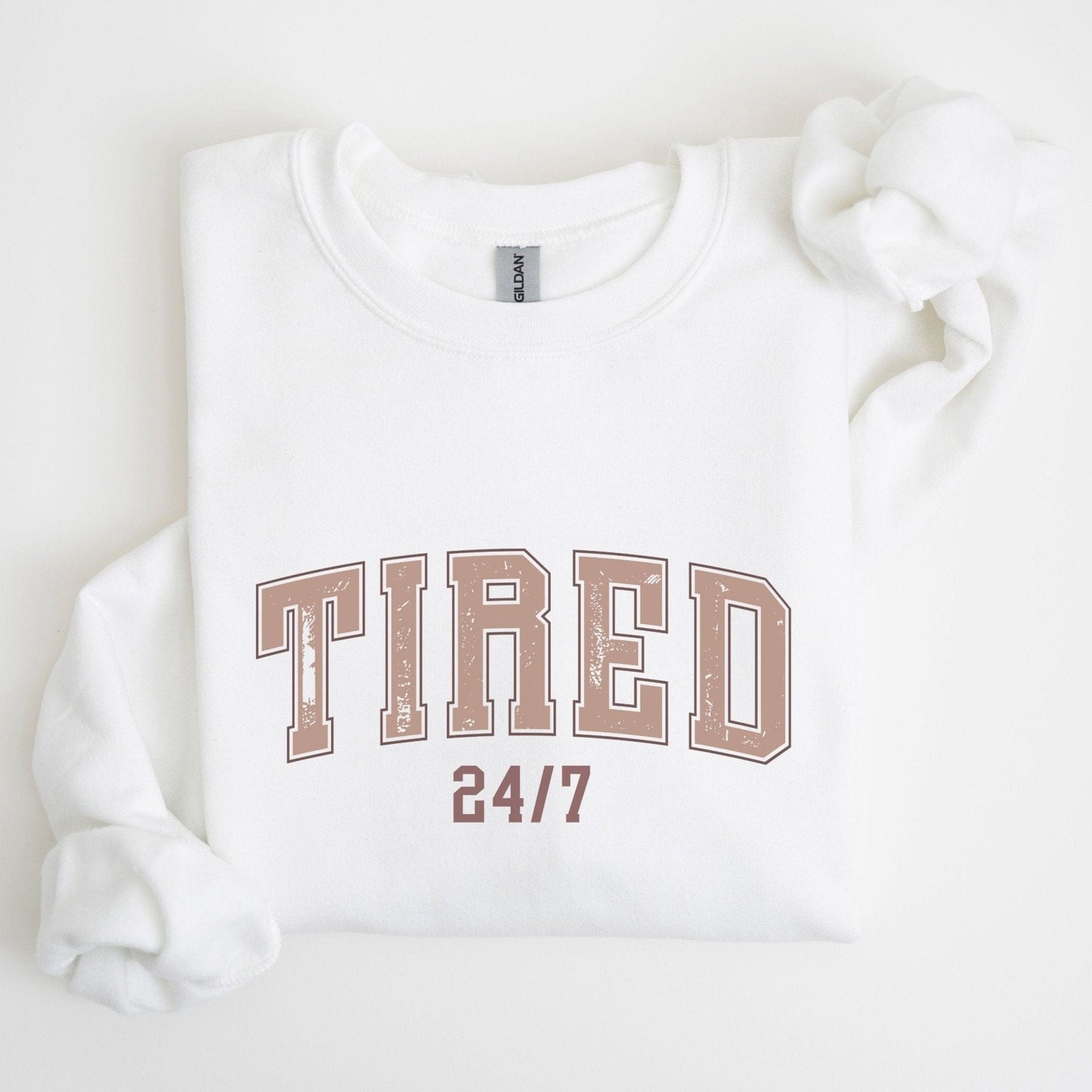 “Tired 24/7” sweatshirt with varsity block letters and a distressed texture — cozy and relatable for the chronically exhausted.