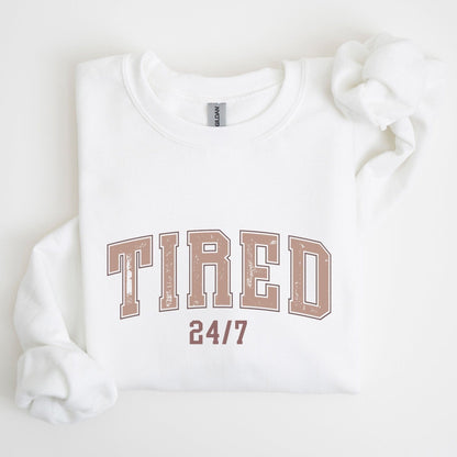 “Tired 24/7” sweatshirt with varsity block letters and a distressed texture — cozy and relatable for the chronically exhausted.