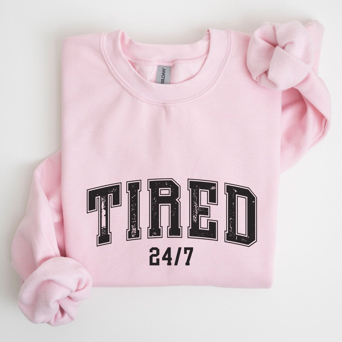 “Tired 24/7” sweatshirt with varsity block letters and a distressed texture — cozy and relatable for the chronically exhausted.