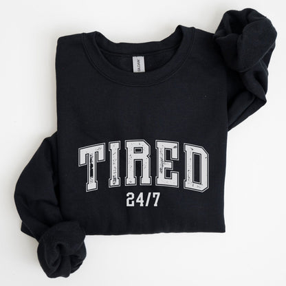 “Tired 24/7” sweatshirt with varsity block letters and a distressed texture — cozy and relatable for the chronically exhausted.