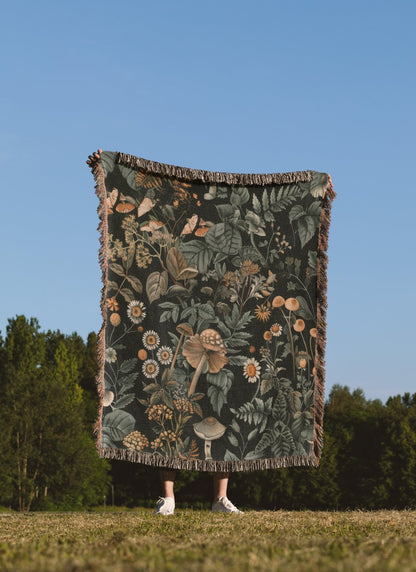 Woodland botanical fringe blanket with mushroom and wildflower print, cozy cottagecore decor.