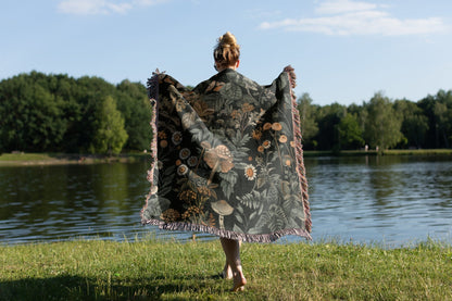 Woodland botanical fringe blanket with mushroom and wildflower print, cozy cottagecore decor.